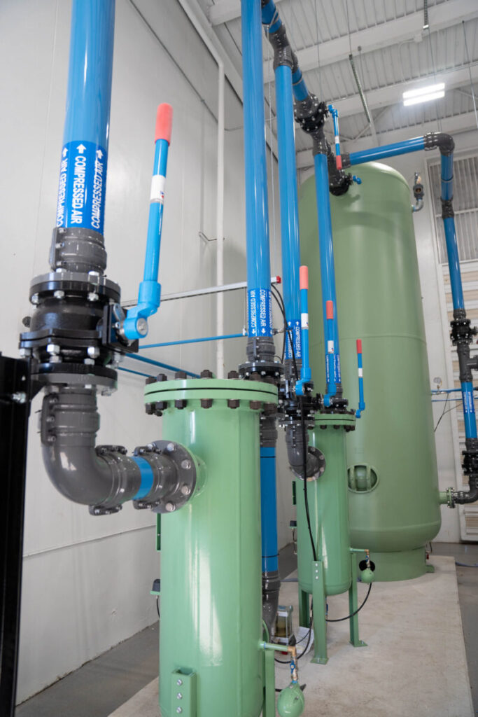 Industrial water filtration system with green tanks and blue pipes in a clean, indoor facility.