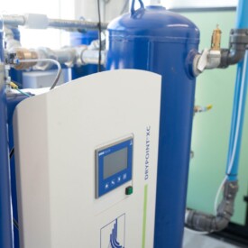 BEKO DRYPOINT XC compressed air dryer system with blue pressure vessel and connected pipes in a bright industrial room.